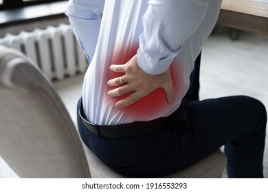 Close Up Of Male Employee In Office Struggle From Lower Back Muscular Pain Or Spasm. Man Worker Sit In Incorrect Posture Suffer From Backache Or Muscle Strain At Workplace. Sedentary Life Concept.