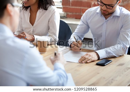 Close up of male employees signing paper contracts during office meeting in boardroom, millennial men put signature on document being hired or employed, workers finalize hiring filling in agreement