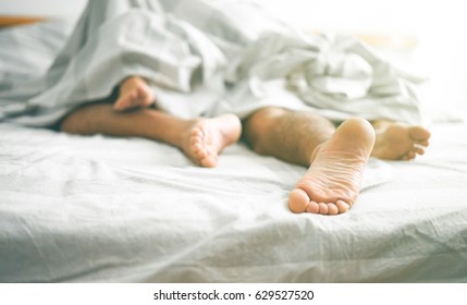 Close up of male and female feet on a bed - Loving couple having sex under white sheets in the bedroom - Concept of sensual and intimate moment of lovers - Vintage filter - Focus on male foot