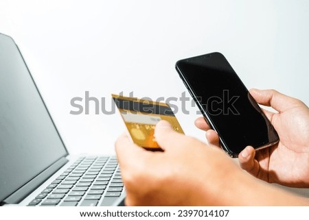 Close up male hand holding a bank credit card doing online transactions using a laptop and smart phone