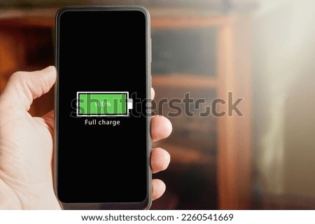 Close up of male hand holding smartphone with full battery icon on the screen indicating that battery level is at one hundred percent. Full charged battery level.