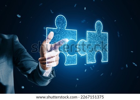 Close up of male hand pointing at glowing digital blue jigsaw puzzle hologram on dark blurry background. Digital solution, collaboration, partners cooperate, implement merge, matching concept