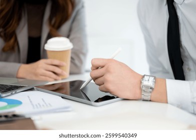 Close de uma mão masculina apontando uma caneta na tela do tablet mostrando dados da empresa para sua colega de trabalho no escritório. Empresário e empresária.