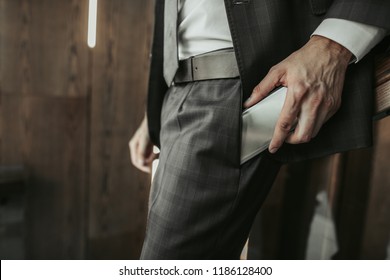 Close up male hand putting contemporary phone in pocket of trousers. He standing indoor