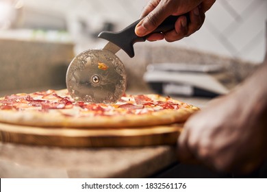Close up of male hand slicing freshly baked pizza with round cutter wheel
