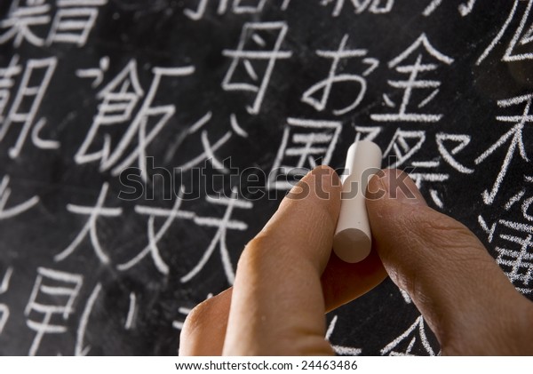 Close up of male hand writing Chinese and\
Japanese characters on blackboard. The words in Japanese have\
random meanings.