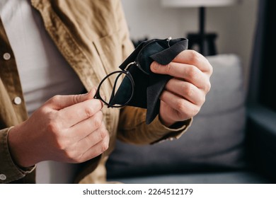 Close up of male hands cleaning eyeglasses with small black cloth sitting alone on cozy couch in living room at home. Cleaning glasses concept - Powered by Shutterstock