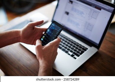 Close up male hands holding big smart phone while connecting to wireless, businessman using technology sitting at modern loft wooden desk, people and modern devices everywhere