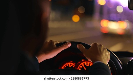 Close up of male hands holding car steering wheel while driving. Man driving automobile at night. Dashboard panel. Fast speed driver. Lights on blurred background in the evening. Traveling concept - Powered by Shutterstock