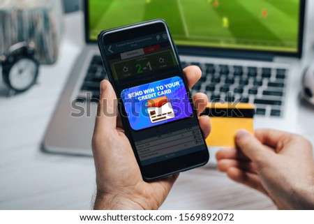 Close up of male hands holding credit card and mobile phone. Man collecting his prize sending money to card after winning it at bookmaker's website betting to his favourite team.