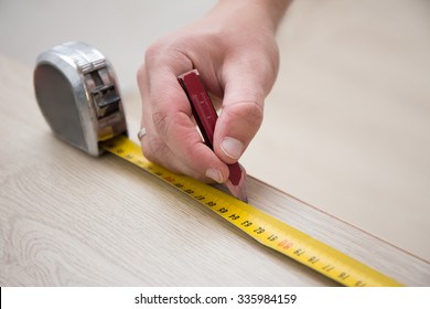 close up of male hands with measuring tape and new laminated wooden floor