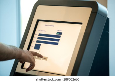 Close up of male hands touching interactive display at self-service transfer machine, doing self-check-in for flight or buying airplane tickets at automatic device in modern airport terminal building