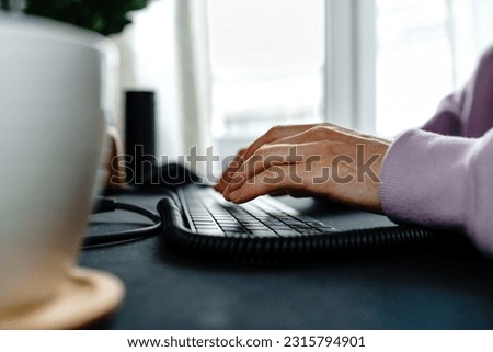 Close up of male hands typing on the computer keyboard while sitting at a desk indoors. no face