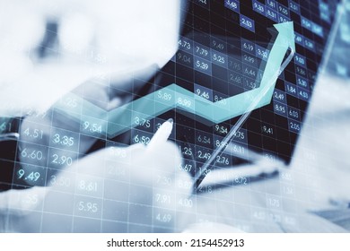 Close up of male hands using tablet and laptop at desktop with creative digital financial numbers or index data on blurry background with growing arrow. Stock market and growth concept.  - Powered by Shutterstock