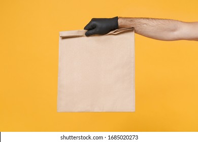 Close up male hold in hand glove brown clear empty blank craft paper bag for takeaway isolated on yellow background. Packaging template mockup. Delivery service concept. Copy space Advertising area