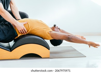 Close Up Of Male Instructor Consulting Handsome African European Beard Man Workout Pilates On Small Barrel Practice In Pilates Studio, Working Out Indoor, Correcting Beginners.