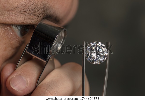 Close up male jeweller. Jeweller looking\
diamond though loupe. Cut and polished diamond. Big size diamond.\
Brilliant, magnifier, tweezers. Diamond\
expert.