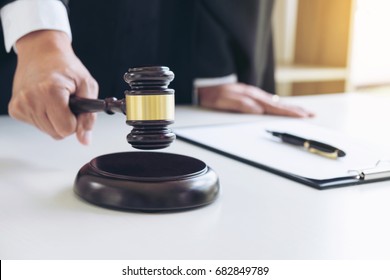 Close up of Male lawyer or judge hand's striking the gavel on sounding block, working with Law books, report the case on table in modern office, Law and justice concept.