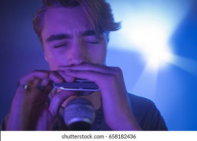 Close up of male musician playing mouth organ in illuminated nightclub - Powered by Shutterstock