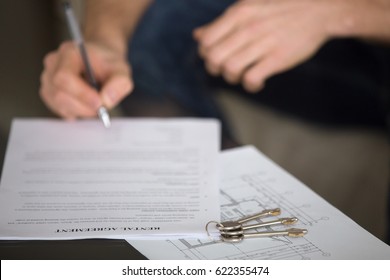 Close Up Of Male Tenant Signing Rental Agreement, Renter With A Pen Putting Signature, Focus On Document And Keys, Young Guy Or Student Decided Live Separately And Found Home For Rent 