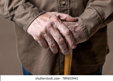 Close up of male wrinkled hands on cane. Isolated on grey background