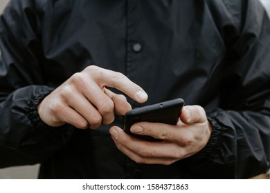 Close Up Of A Man In Black Raincoat Typing On A Smartphone. 