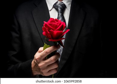 close up of man in black suit holding red rose.