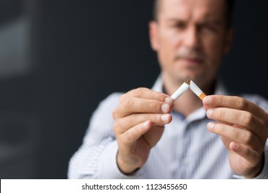 Close Up Of Man Breaking Cigarette In Half.  Quitting Smoking Habit.