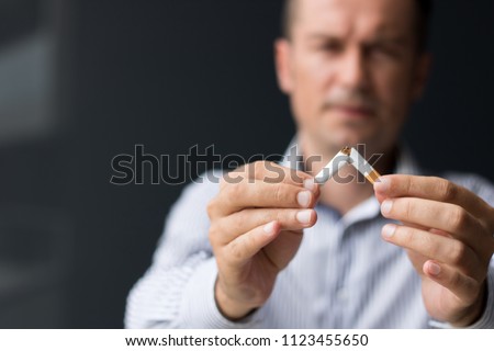 Close up of man breaking cigarette in half.  Quitting smoking habit.