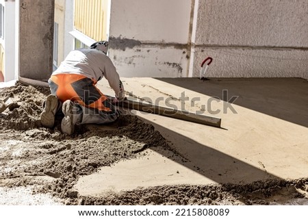 Close up of man builder placing screed rail on the floor covered with sand-cement mix at construction site. Male worker leveling surface with straight edge while screeding floor. Blurred background Stock photo © 