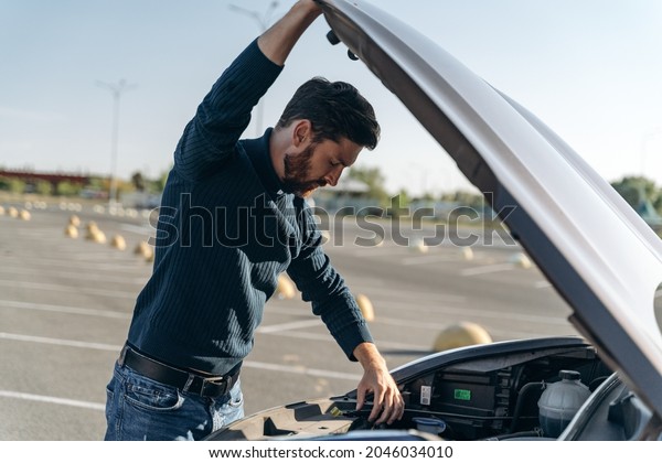 Close up of man with a car problem. Confused man in\
a casual closes examines the car engine while standing at the road.\
Stock photo