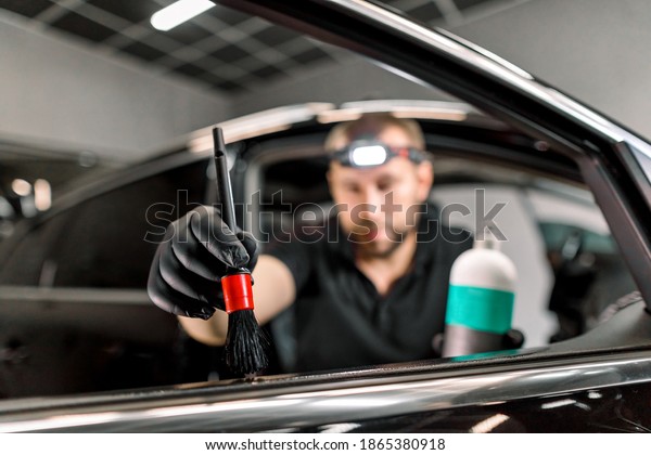Close up of man, car service station worker, making\
cleaning and care procedures for car door interior, using brush and\
special cream or milk for leather care and remowing scratches.\
Focus on hand