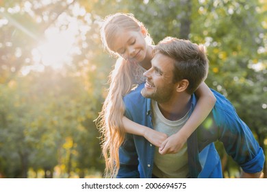 Close up of a man carrying his daughter on his back outdoors. Small young daughter sitting piggyback on her father daddy in a park forest wood - Powered by Shutterstock