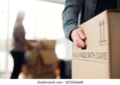 Close Up Of Man Carrying Removal Box As Couple Move In Or Out Of New Home Together