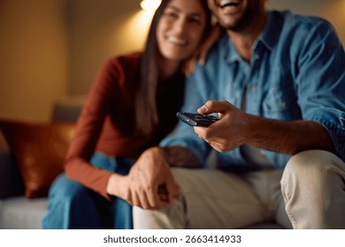 Close up of man changing channels while watching TV with is girlfriend at home. 