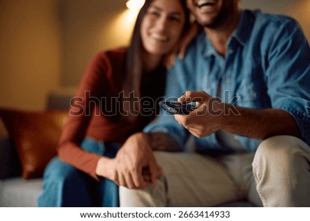 Close up of man changing channels while watching TV with is girlfriend at home. 