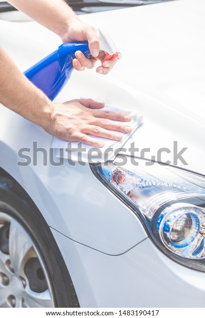 Close up\
of man cleaning car hood and headlights with cloth and spray\
bottle, car maintenance concept. Space for\
copy.