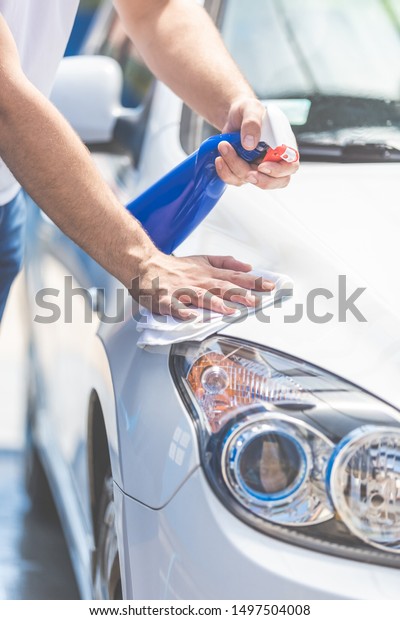 Close up
of man cleaning car hood and headlights with cloth and spray
bottle, car maintenance concept. Space for
copy.