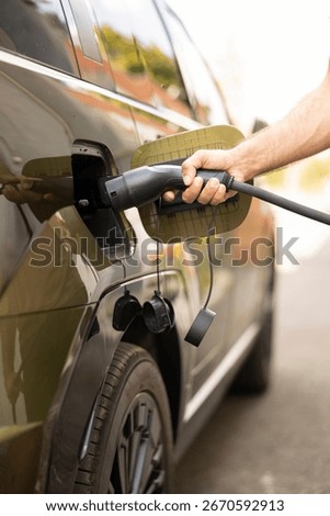 Close up of man connecting cable to EV vehicle inlet port charging at station. Driver opening charging port flap, plugging electric car into charger, reducing greenhouse gas emissions