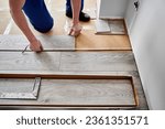 Close up of man construction worker checking distance from wall to laminate board. Male builder using tape measure while installing laminate flooring in apartment under renovation.