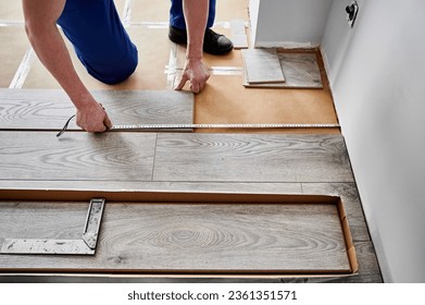 Close up of man construction worker checking distance from wall to laminate board. Male builder using tape measure while installing laminate flooring in apartment under renovation.