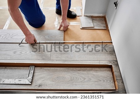 Close up of man construction worker checking distance from wall to laminate board. Male builder using tape measure while installing laminate flooring in apartment under renovation.