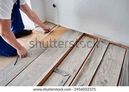 Close up of man construction worker checking distance from wall to laminate board. Male builder using tape measure while installing laminate flooring in apartment under renovation.