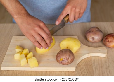close up of a man cutting a peeled potato in dices on a wood cutting board