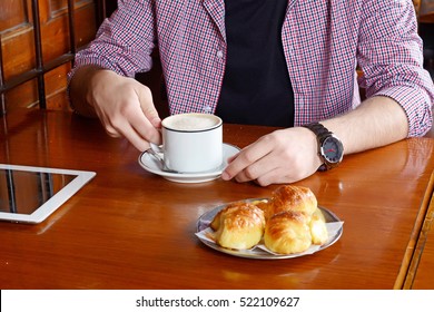 Close up of a man with digital tablet and drinking coffee at a cafe. Indoors.