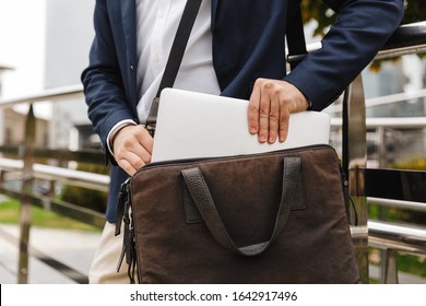 Nahaufnahme eines Mannes in formaler Kleidung, der seinen Laptop aus der Tasche holt, während er im Freien steht