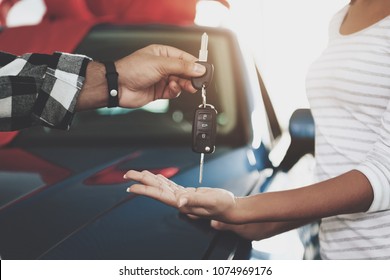 Close up man is giving keys to woman. African american family at car dealership. Father, mother and son near new blue car.