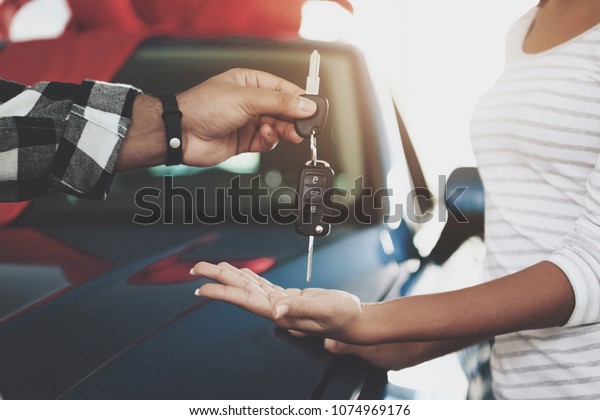 Close up man is giving keys to woman. African\
american family at car dealership. Father, mother and son near new\
blue car.