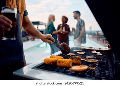 Close up of man grilling meat on barbecue while gathering with friends at pool party.  - Powered by Shutterstock