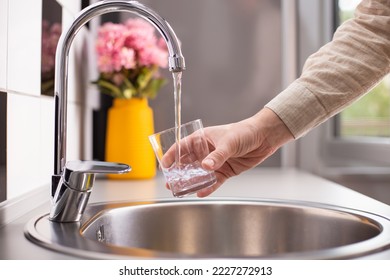 Close up of a man hand filling a glass of water directly from the tap. Filling glass of water from the tap at home. - Powered by Shutterstock